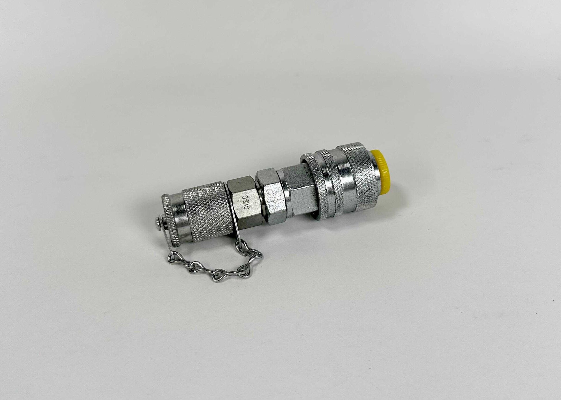 A G1/4" to Stauff Male Adaptor with a hex nut, yellow capped end, and short attached chain lies on a plain white surface.