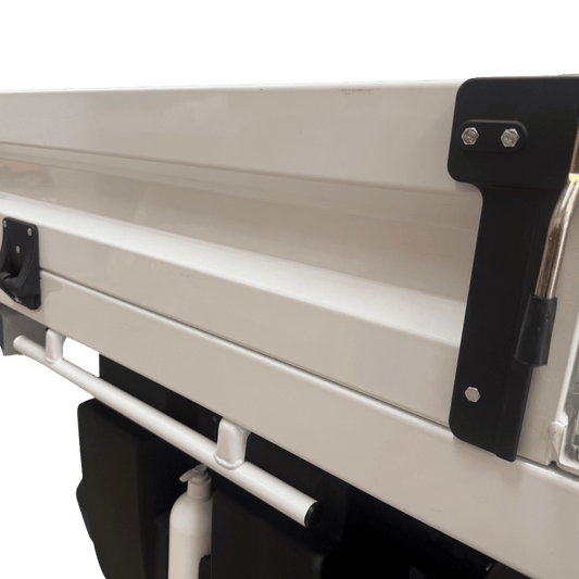 Exterior rear view of a white ute tray fitted with the 30mm tray side shortening component, showing the black mounting bracket secured with two silver bolts and the chrome handle in the upright/locked position.