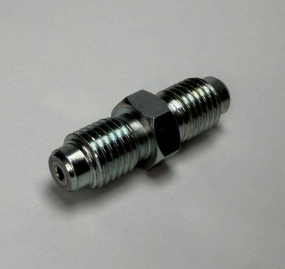 A Stauff Joiner, a metal double-ended threaded pipe fitting with a hexagonal middle section, is placed on a plain light surface.