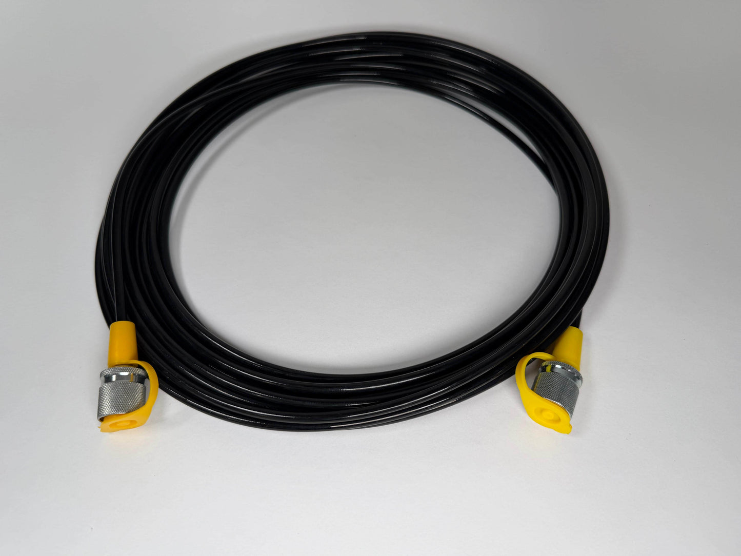 A coiled Stauff to Stauff style test hose (5m) from Stauff, with black cable and yellow-silver metal ends, displayed on a plain white surface.